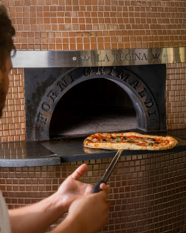Une pizza sur la pelle, à l'entrée du four à bois