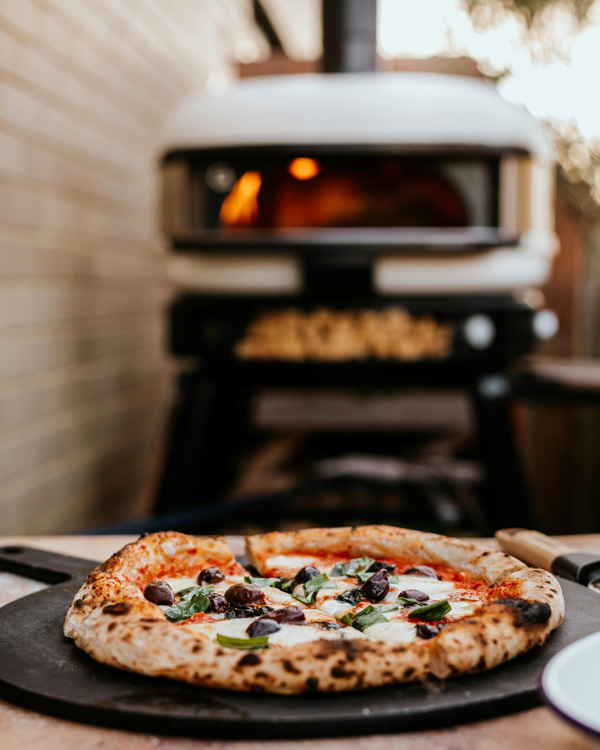 Une pizza sortie du four à bois, posée sur une planche