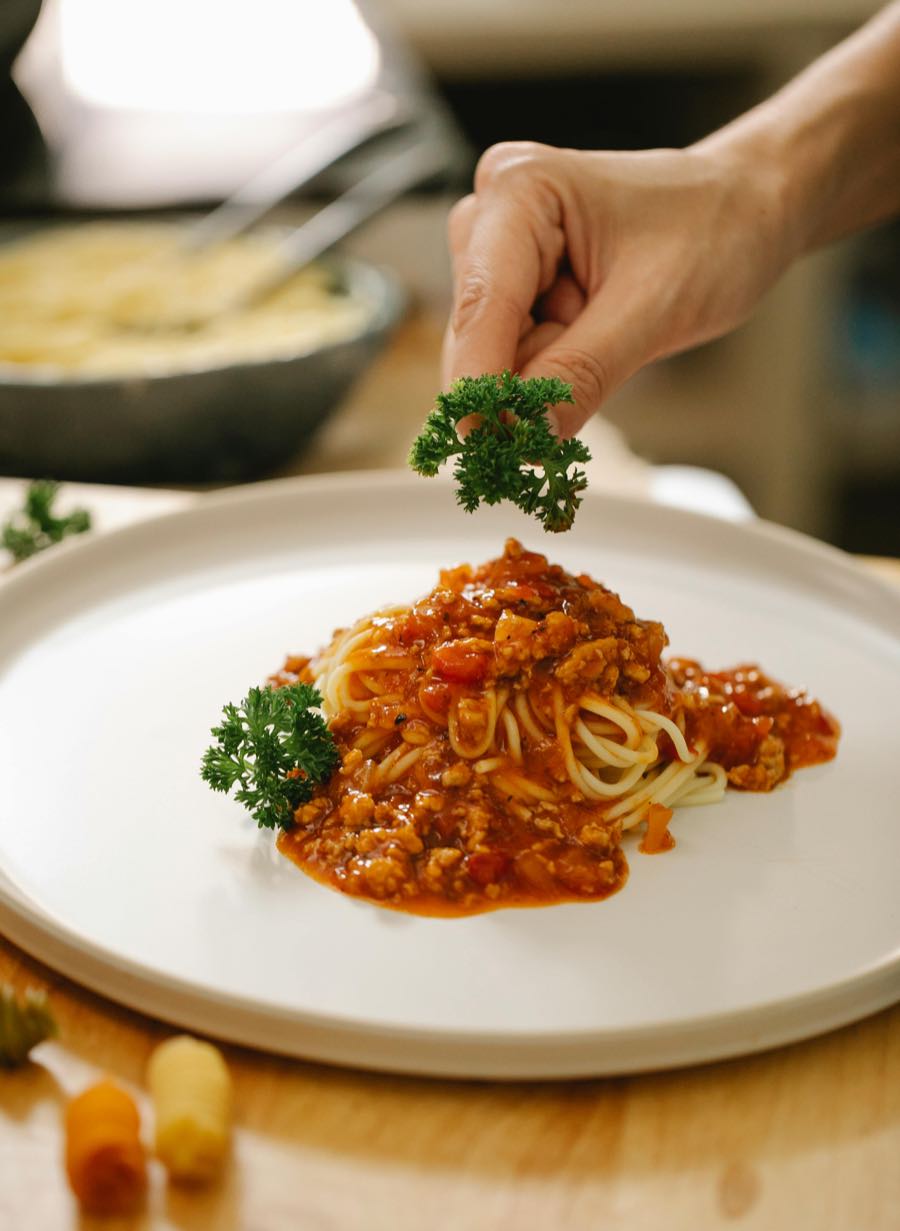 Un cuisinier dépose du persil sur une assiette de pâtes