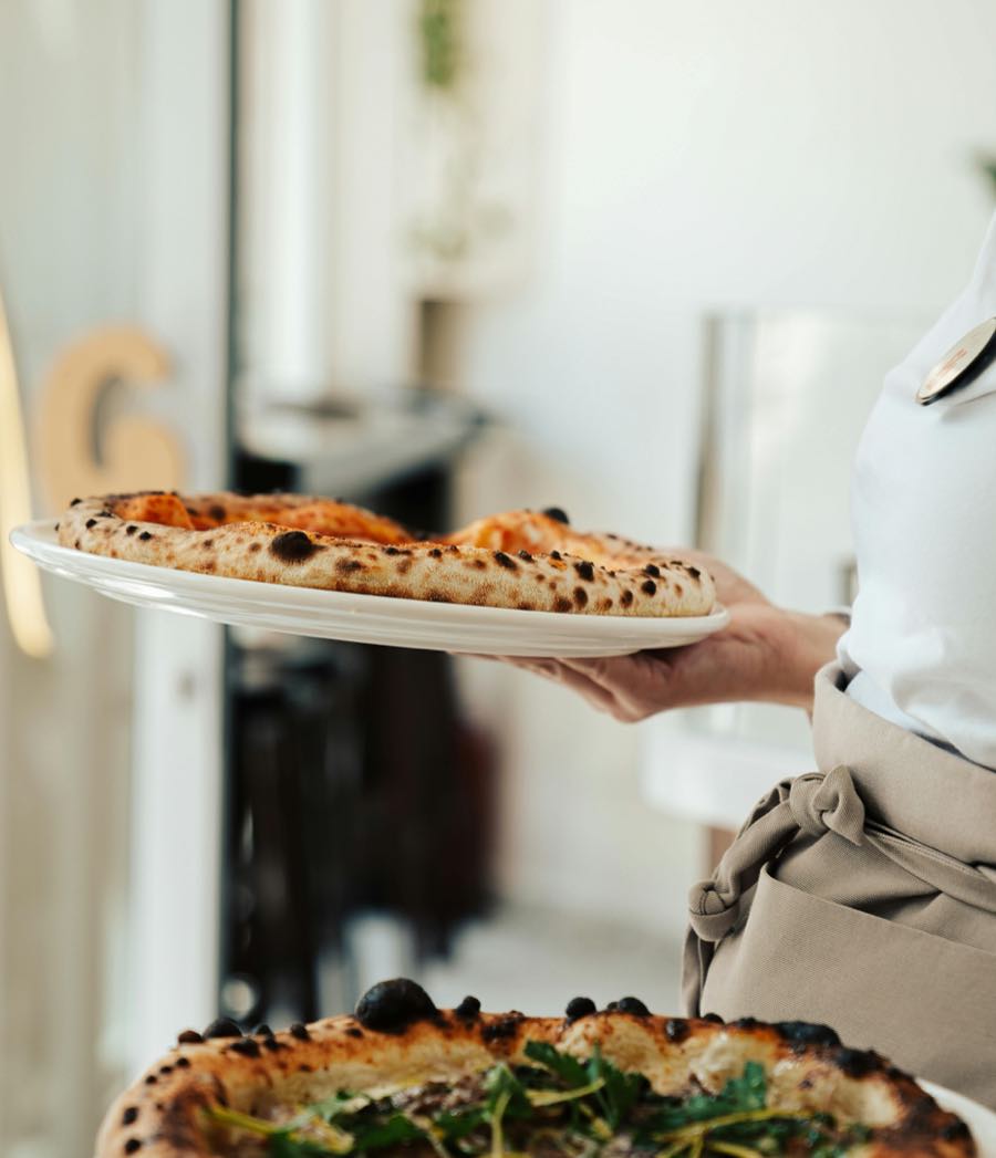 Une serveuse apporte une pizza cuite au feu de bois